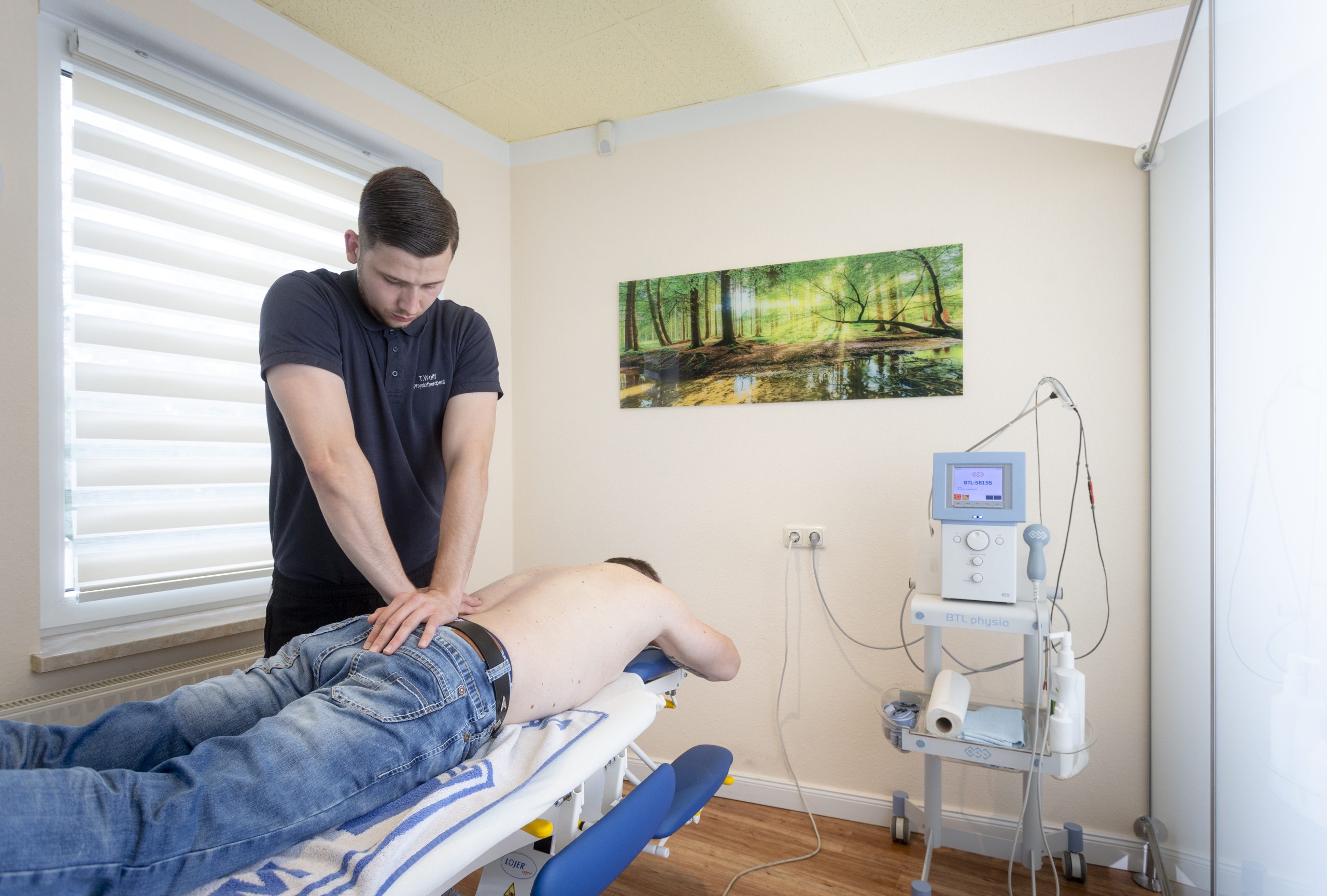 Ein Therapeut behandelt den Rücken eines Patienten, welcher auf einer Liege liegt.