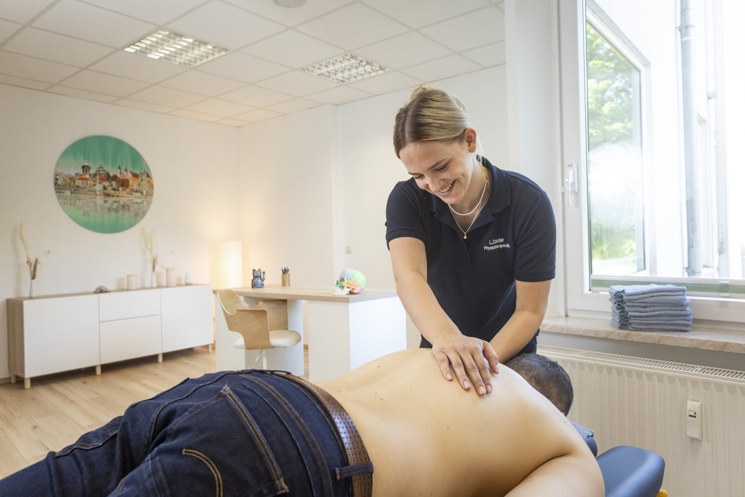 Ein Therapeut behandelt den Rücken eines Patienten, welcher auf einer Liege liegt.